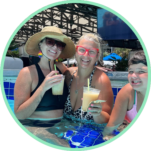 Three women in a pool, smiling and holding drinks.